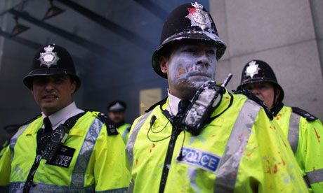 Paint-splattered police officers look on as protesters attack Topshop on Oxford Street during the anti-cuts march in London
